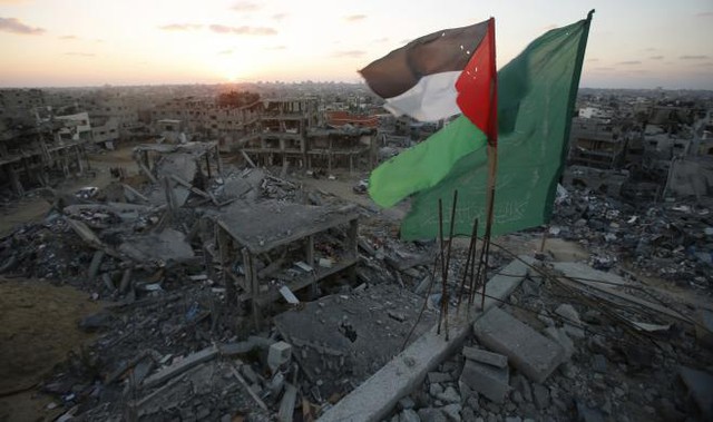 Cờ Palestine và cờ của nhóm vũ trang Hamas tung bay trên đỉnh một tòa nhà bị tàn phá trong cuộc không kích của quân đội Israel vào thành phố Gaza.