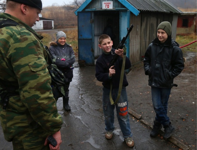 Cậu bé cầm súng đứng bên ngoài một hầm tránh bom ở thành phố Donetsk, Ukraine.