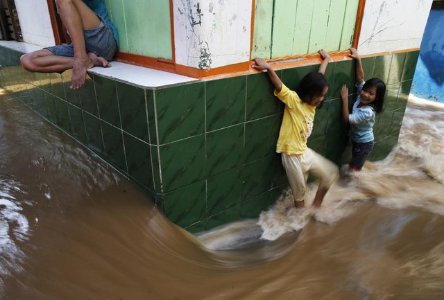 Trẻ em cố gắng đi qua đường phố ngập lụt tại khu dân cư Kampung Melayu ở Jakarta, Indonesia.