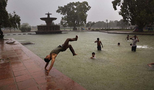 Một cậu bé nhảy nhào lộn dưới trời mưa ở New Delhi, Ấn Độ.