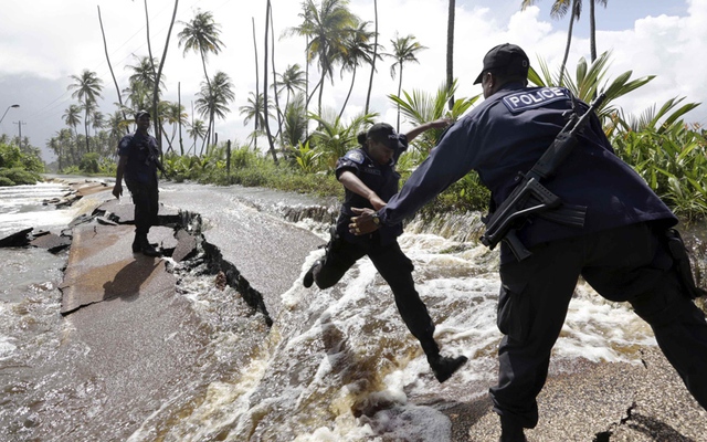 Cảnh sát nhảy qua một đoạn đường bị hư hỏng do nước lũ ở Manzanilla, Trinidad.
