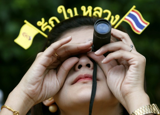Một phụ nữ dùng ống nhòm để cố gắng nhìn thấy Nhà vua Thái Lan đang dưỡng bệnh tại bệnh viện Siriraj ở Bangkok, nhân sinh nhật lần thứ 87 của ông.