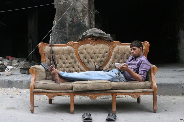 Chiến binh phiến quân Syria sử dụng điện thoại thông minh trong khi nằm trên ghế sofa ở thành phố Aleppo.