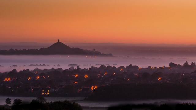 Mặt trời lặn phía sau ngọn đồi Glastonbury Tor khi sương mù bao phủ mặt đất ở Somerset, Anh.