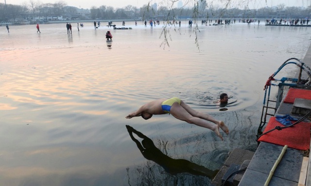 Người đàn ông nhảy xuống nước lạnh, trong khi những người khác chơi hockey trên phần nước đóng băng của hồ Houhai ở Bắc Kinh, Trung Quốc.