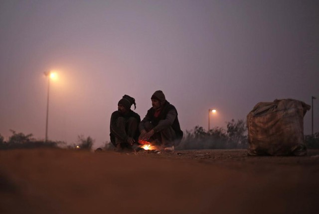 Mọi người ngồi sưởi ấm quanh đống lửa trên đường phố trong buổi sáng lạnh ở New Delhi, Ấn Độ.