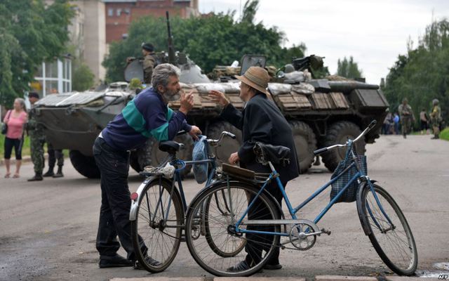Người dân địa phương đứng nói chuyện trước một xe bọc thép chở quân của quân đội Ukraine trên đường ở thành phố Slavyansk.
