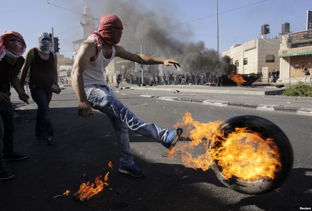 Một người biểu tình Palestine đá chiếc lốp xe cháy về phía cảnh sát Israel trong cuộc đụng độ tại Shuafat, ngoại ô thành phố Jerusalem.