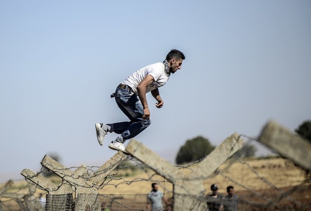 Một người Kurd nhảy qua hàng rào vào lãnh thổ Syria trong cuộc biểu tình ở Suruc, biên giới giữa Thổ Nhĩ Kỳ và Syria.