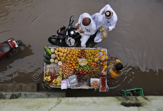 Mọi người mua trái cây từ một người bán hàng rong trên đường phố ngập nước sau mưa lớn ở thành phố Ahmedabad, Ấn Độ.