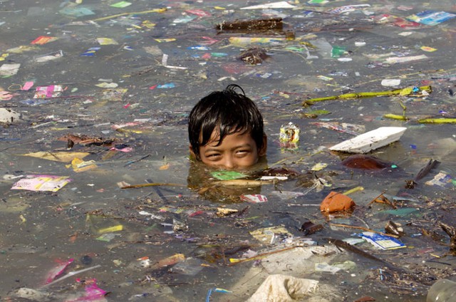 Cậu bé bơi giữa biển rác bao phủ mặt nước tại vịnh Manila, Philippines.