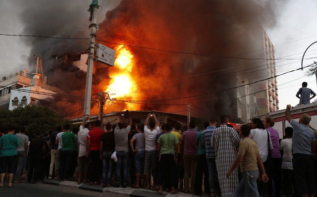 Mọi người đứng xem một tòa nhà bốc cháy sau khi bị quân đội Israel không kích tại thành phố Gaza.