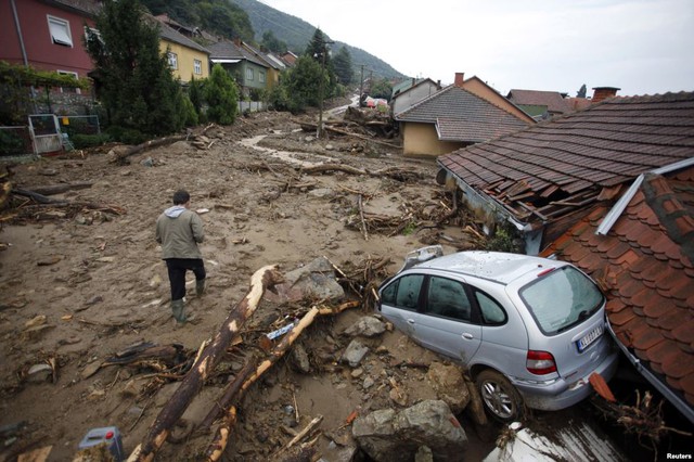 Người đàn ông đi qua chiếc ô tôi bị phá hủy trên đường bao phủ đầy bùn đất do mưa lớn tại ngôi làngTekija, Serbia.