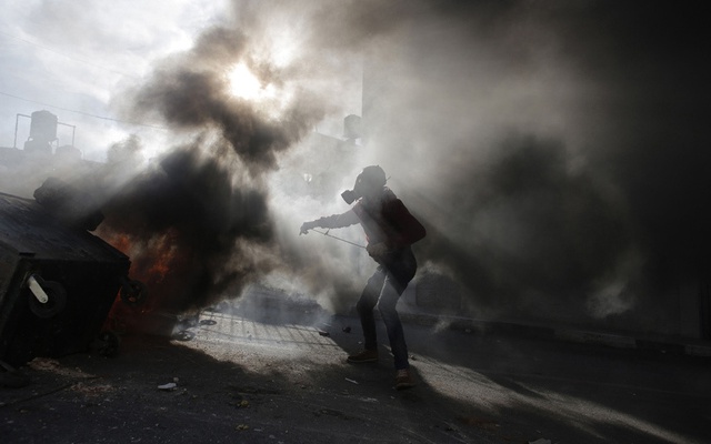 Người biểu tình Palestine đeo mặt nạ, đứng giữa khói hơi cay do quân đội Israel bắn ra trong cuộc đụng độ ở thành phố Ramallah, Bờ Tây.