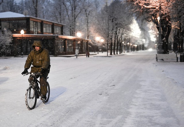 Người đàn ông đạp xe dưới mưa tuyết trong công viên Gorky ở Moscow, Nga.