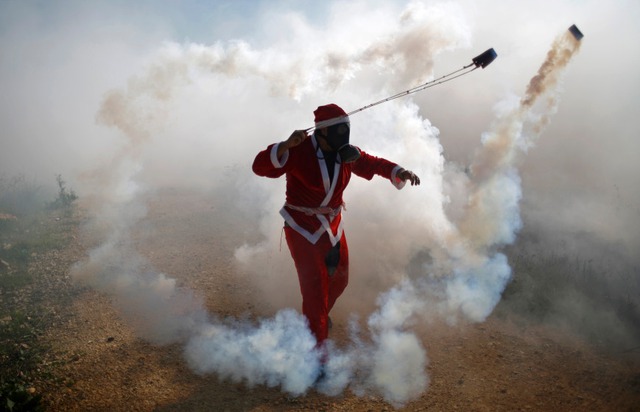 Người biểu tình Palestine mặc trang phục ông già Noel ném lựu đạn hơi cay trả lại binh lính Israel ở Bilin, Bờ Tây.