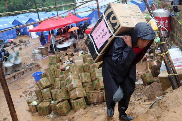 Tình nguyện viên vác hàng hóa cứu trợ tại một khu định cư tạm thời, sau trận động đất mạnh 6,5 độ ricter tại tỉnh Vân Nam, Trung Quốc.