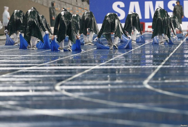 Các thành viên của ban tổ chức sử dụng khăn để thấm nước mưa trên đường chạy trước nội dung chung kết chạy 100m nam và nữ tại Đại hội thể thao châu Á ở Incheon, Hàn Quốc.