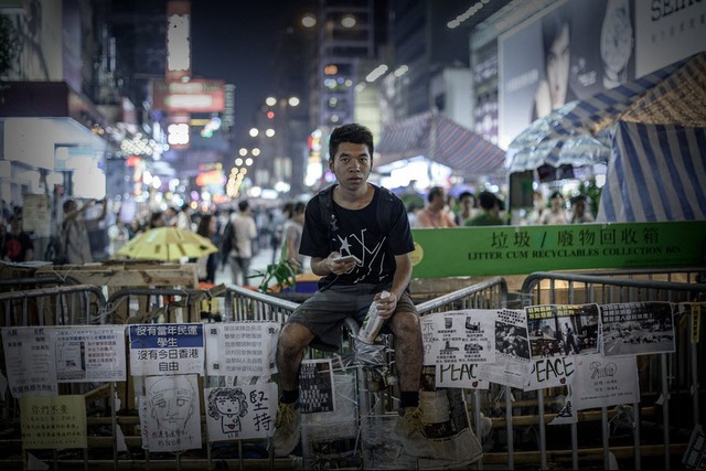 Người biểu tình ngồi trên hàng rào chắn tại khu phố thương mại Mong Kok, Hong Kong.