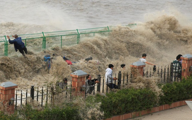 Khách du lịch trèo lên hàng rào để tránh sóng thủy triều dâng cao trên sông Tiền Đường ở Hàng Châu, Trung Quốc.