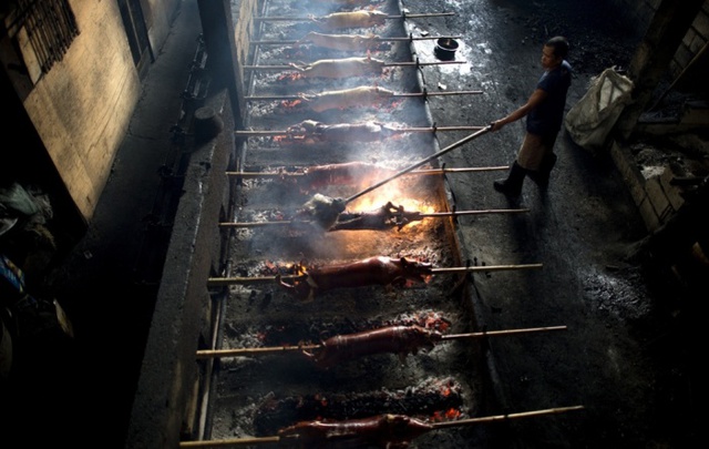 Công nhân tưới dầu ăn lên những con lợn đang được quay trên than hoa ở Manila, Philippines. Lợn quay là món ăn phổ biến nhất ở Philippines trong dịp lễ Giáng sinh và Năm mới.