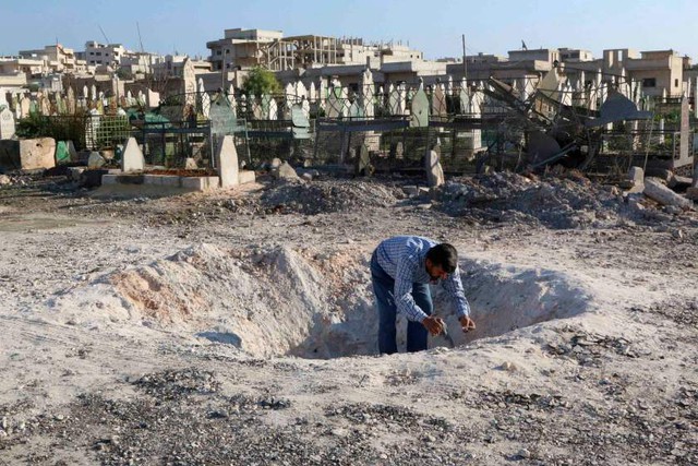 Người đàn ông kiểm tra một hố lớn trên mặt đất sau đợt không kích ở Sheikoun, Syria.