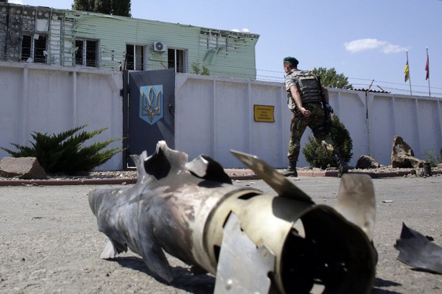 Lính biên phòng Ukraine đi qua vỏ một quả rocket bên ngoài một trạm kiểm soát ở vùng Lugansk.