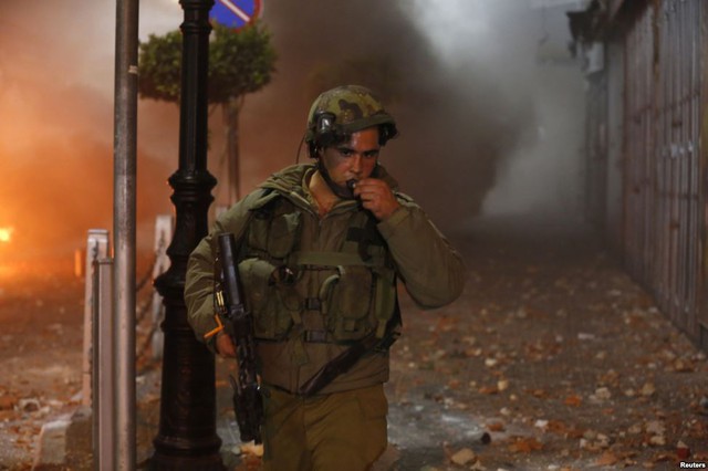 Một binh sĩ Israel đi qua hiện trường cuộc đụng đội với những người biểu tình Palestine ở thành phố Ramallah, Bờ Tây.