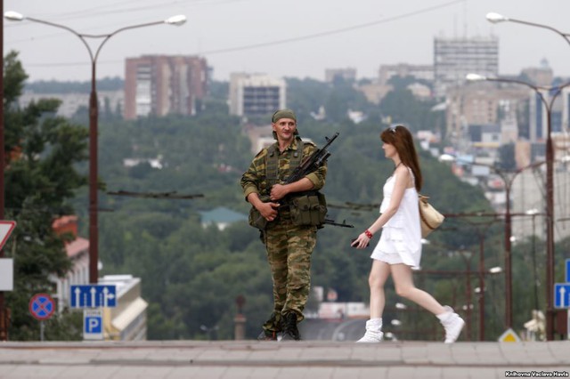 Thiếu nữ đi ngang qua một tay súng ly khai thân Nga đứng bảo vệ trên đường phố ở Donetsk, Ukraine.
