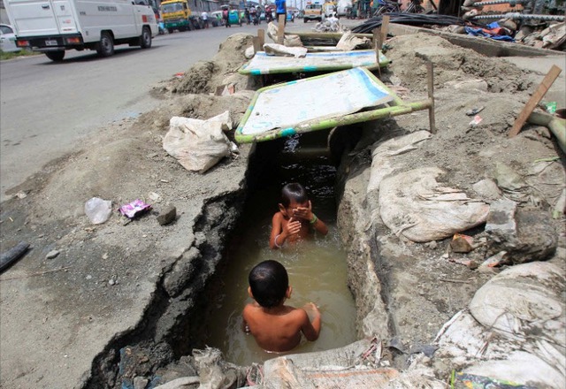 Trẻ em tắm dưới cống thoát nước lộ thiên ở Manila, Philippines.