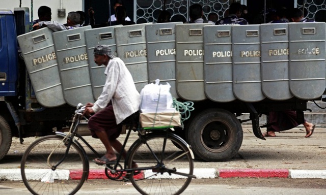 Người đàn ông đạp xe qua đội cảnh sát tuần tra trên đường phố ở Yangon, Myanmar.