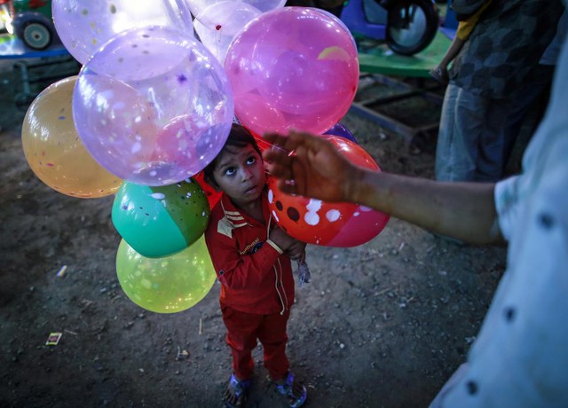 Cậu bé 5 tuổi giúp bố bán bóng bay tại một hội chợ ở Mumbai, Ấn Độ.