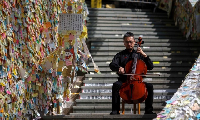 Nghệ sĩ cello David Wong biểu diễn trước một bức tường dán đầy thông điệp của những người biểu tình tại quận Admiralty, Hong Kong.