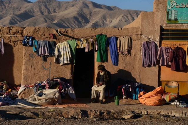 Người bán quần áo chờ khách hàng tới mua bên ngoài một ngôi nhà bằng đất ở Herat, Afghanistan.