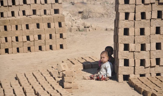 Trẻ em ngồi chơi trên nền đất trong một nhà máy sản xuất gạch ở Jawzjan, Afghanistan.
