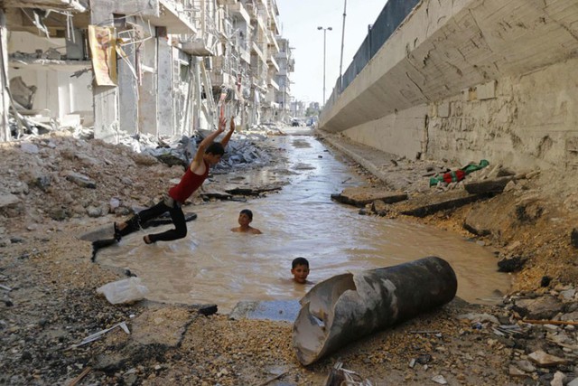 Trẻ em tắm dưới một hố bom trên đường phố ở Aleppo, Syria.