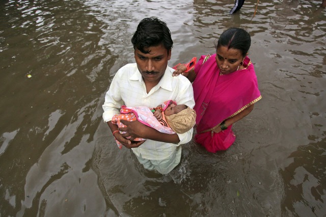 Một cặp vợ chồng bế con mới sinh lội qua đường phố ngập lụt sau mưa lớn ở Ahmedabad, Ấn Độ.