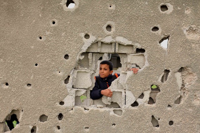 Cậu bé người Palestine nhìn qua lỗ trên tường tại thành phố Gaza.