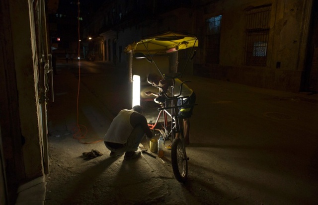 Người lái taxi xe đạp sửa phương tiện trong đêm ở thành phố Havana, Cuba.