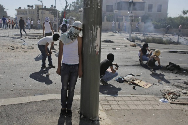 Một thanh niên người Palestine nấp sau cột điện trong cuộc đụng độ với cảnh sát Israel tại Jerusalem.