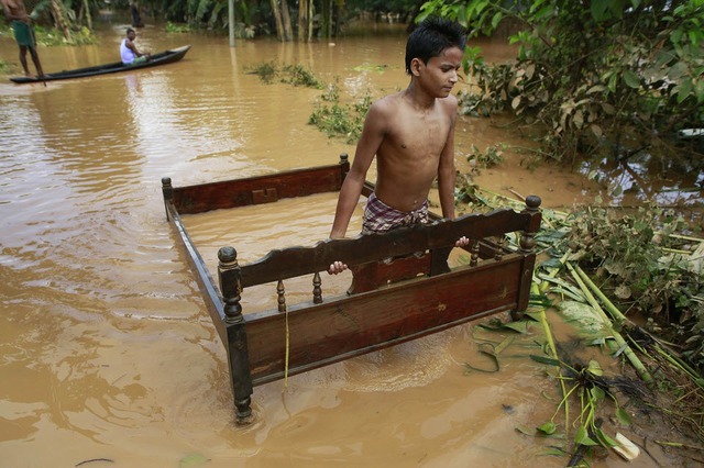 Cậu bé di chuyển giường ngủ qua nước lũ ở Krishnai, Ấn Độ.