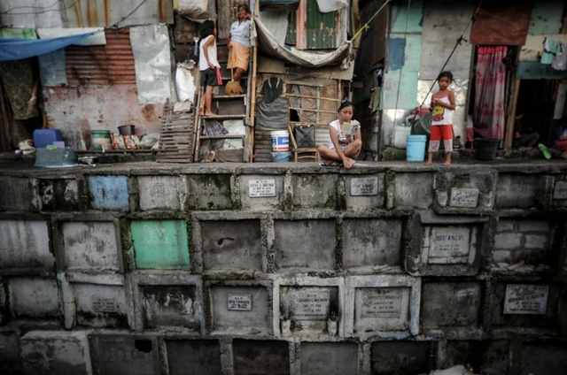 Người phụ ngồi đọc sách bên ngoài nhà cô, được xây dựng trên một nghĩa trang ở Navotas, Philippines.