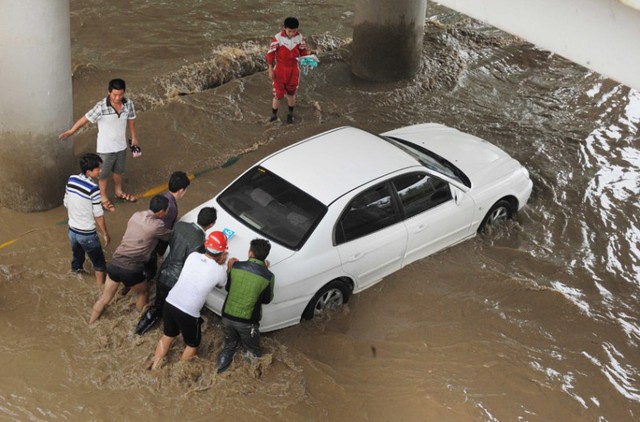 Mọi người giúp đỡ đẩy một chiếc ô tô mắc kẹt trên đường phố ngập lụt ở thành phố Quý Dương, Trung Quốc.