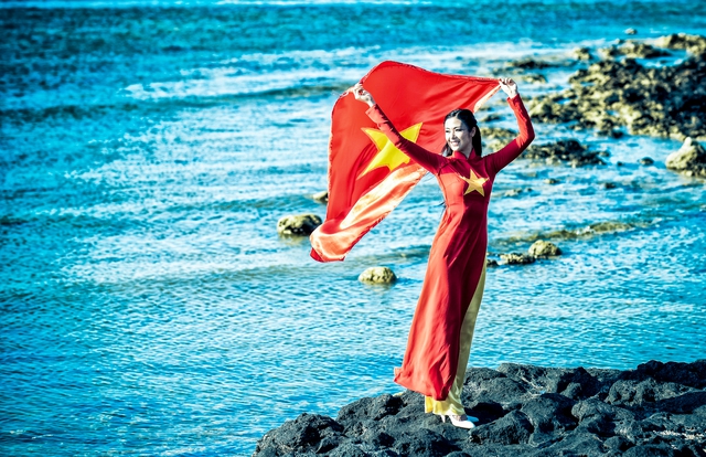Hoa Hậu Ngọc Hân cùng lá cờ tung bay trước biển.