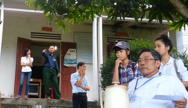 Ông Nguyễn Trọng Tranh (người áo xanh, quần xanh bên trái) đứng trước phòng làm việc chỉ tay đe nẹt và dọa đập máy của PV.
