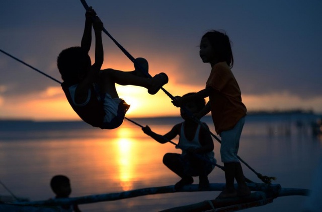 Trẻ em chơi trên chiếc thuyền đánh cá bằng gỗ dưới hoàng hôn ở Guiuan, Philippines.