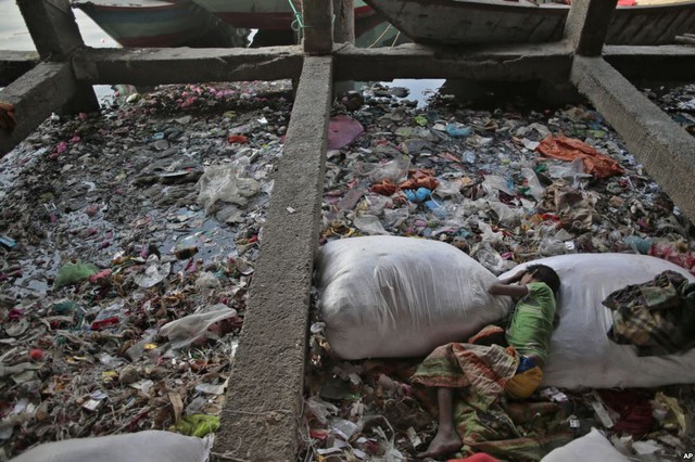 Em bé vô gia cư nằm ngủ trên túi rác cạnh dòng sông Buriganga ô nhiễm ở thành phố Dhaka, Bangladesh.