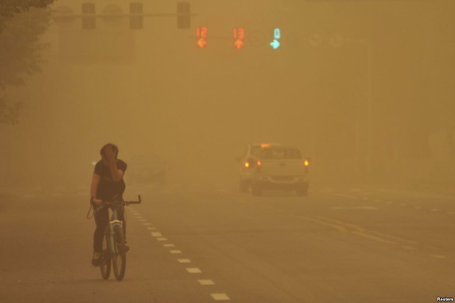 Nam thanh niên dùng tay che mặt đạp xe trên đường phố trong bão cát ở thành phố Ngũ Gia Cừ, khu tự trị Tân Cương, Trung Quốc.
