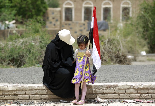 Người phụ nữ Yemen và con gái cầm cờ ngồi nghỉ ngơi trên một bức tường trong cuộc biểu tình phản đối các cuộc không kích của liên quân Ả-rập nhằm vào nhóm phiến quân Huthi ở thủ đô Sanaa.