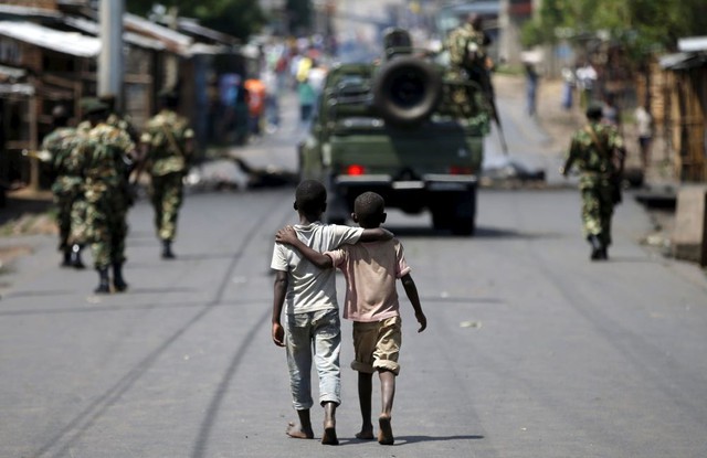 Hai cậu bé khoác vai nhau đi sau các binh sĩ tuần tra trên đường phố ở Bujumbura, Burundi.